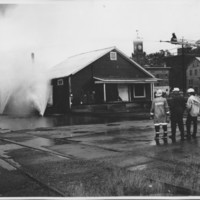 Removal of the B. and M. Freight House by Burning and as a Fire Fighter&#039;s Training Exercise. 7/12/1975. Neighboring Buildings Safe Behind Water Fans.